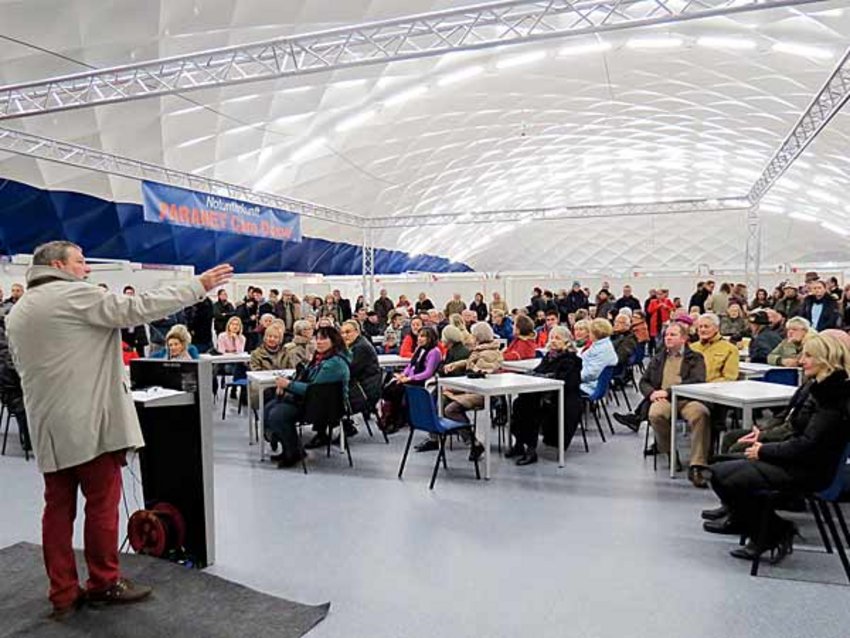 Traglufthalle Unterfoehring Besucher Foto: Ernst Weidenbusch, Stellvertreter des Landrats, spricht zu den zahlreichen Besuchern, die in die Traglufthalle gekommen sind. Sie sitzen auf den Stühlen im Aufenthaltsbereich oder stehen an den Seiten des Aufenthaltsbereiches.