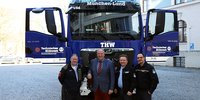 Im Hintergrund frontal das neue Wechselladerfahrzeug in Blau. Beide Türen des Führerhauses sind geöffnet. Davor stehen vier Männer, von links nach rechts: Andreas Zanker (THW), Landrat Christoph Göbel, Christian Dietrich (THW) und Julian Pfeuffer (THW)