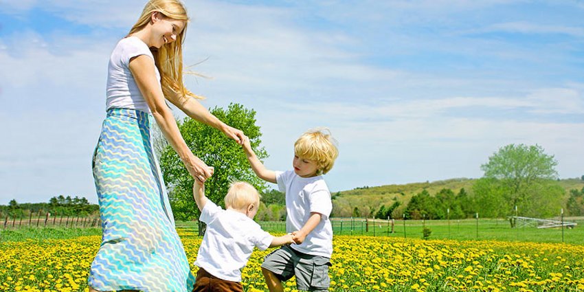 Tanzende Frau mit zwei Kleinkindern im Blumenfeld bei sonnigem Wetter