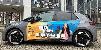 Ein Auto, VW id3, mit Folierung im Stil der neuen Arbeitgebermarke des Landkreises steht seitlich vor dem Haupteingang des Landratsamts.