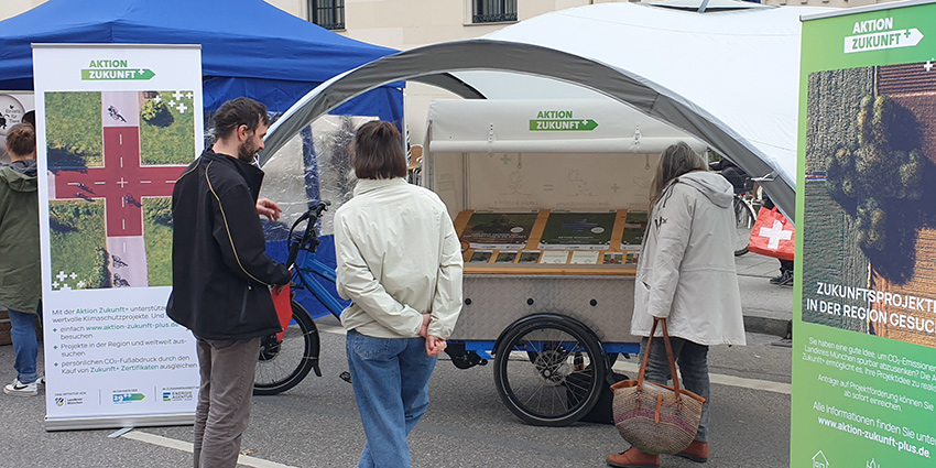 Die Aktion Zukunft+ auf dem Zamanand-Festival Foto: Drei Personen betrachten den Infostand der Aktion Zukunft+ auf dem Zamanand-Festival in München